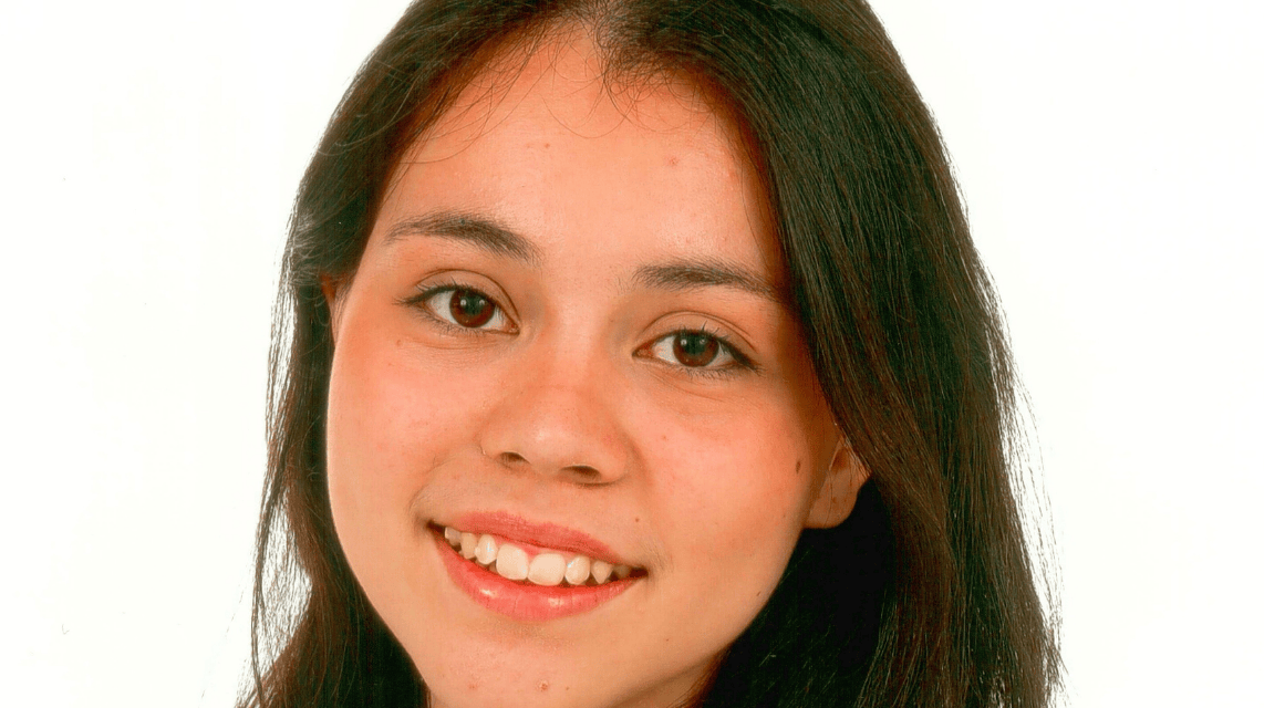 Headshot of a young woman with straight dark brown hair, warm brown eyes, and a friendly smile, photographed against a plain white background.